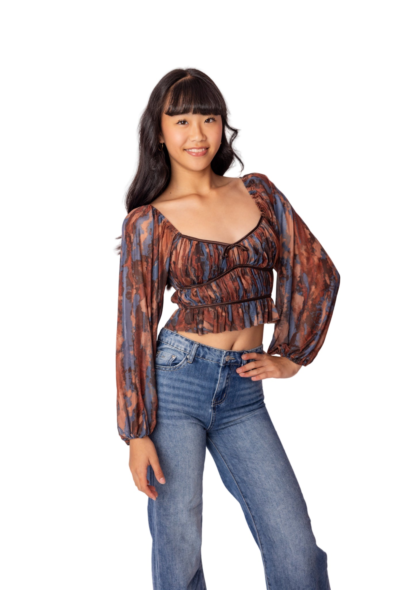 Woman wearing a patterned top and blue jeans on a white background