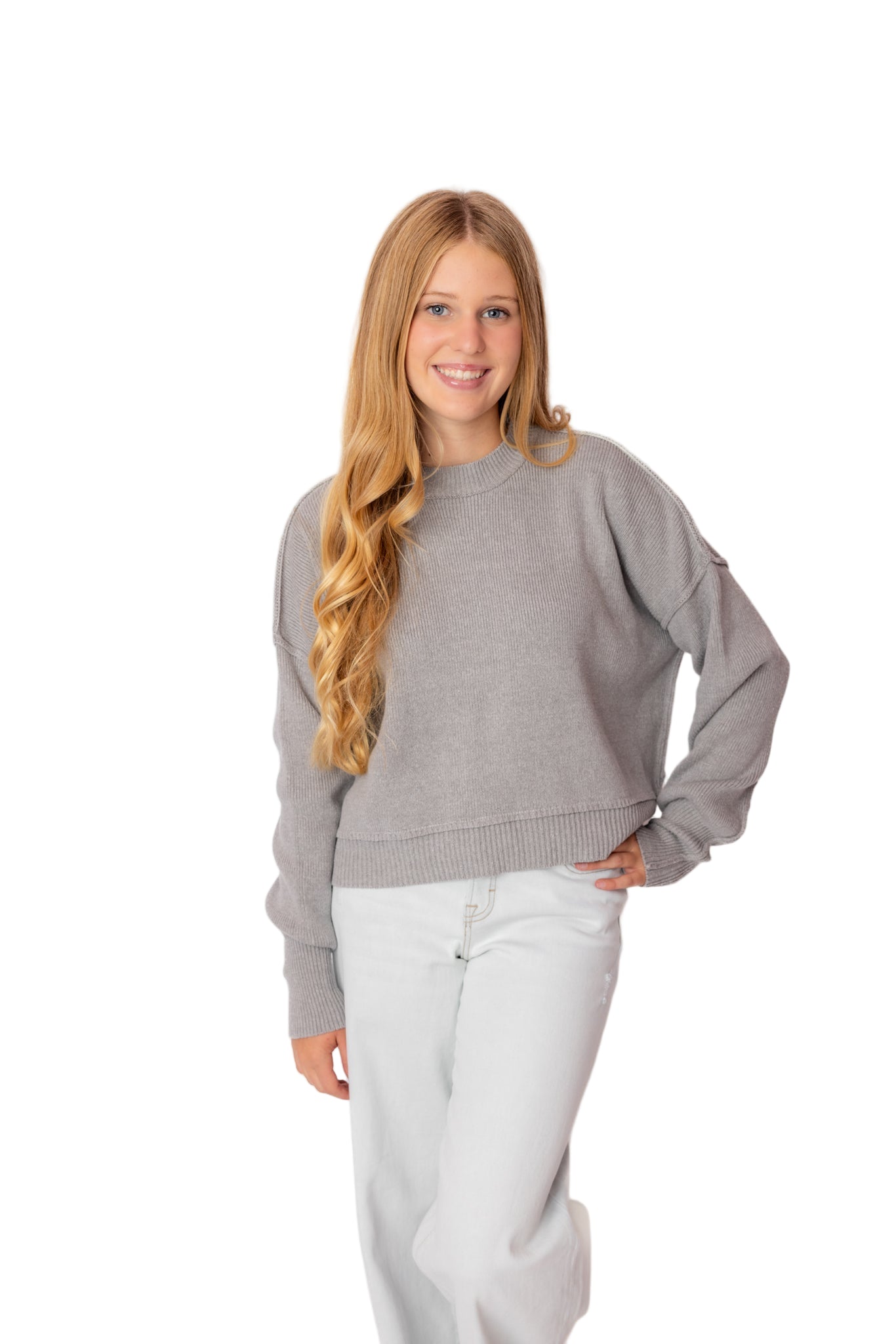 Woman wearing a gray sweater and white pants against a white background